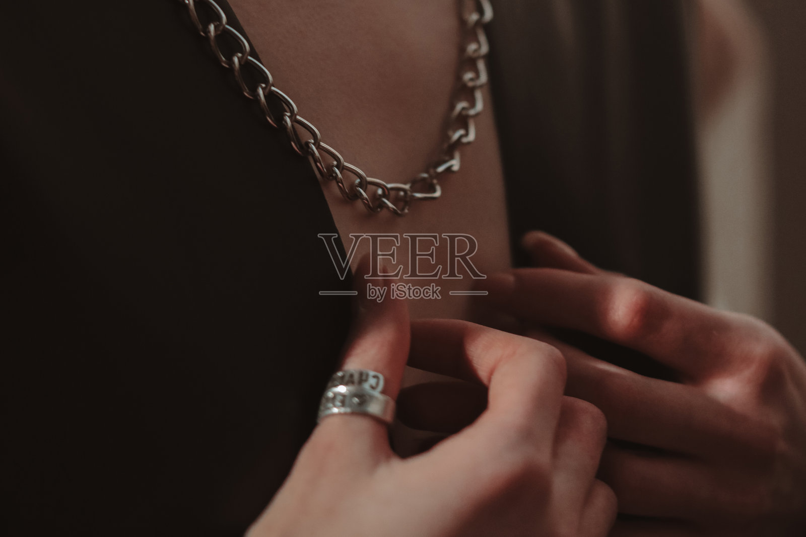 女性的手，银链挂在脖子上的女人穿着一件黑色夹克。照片摄影图片