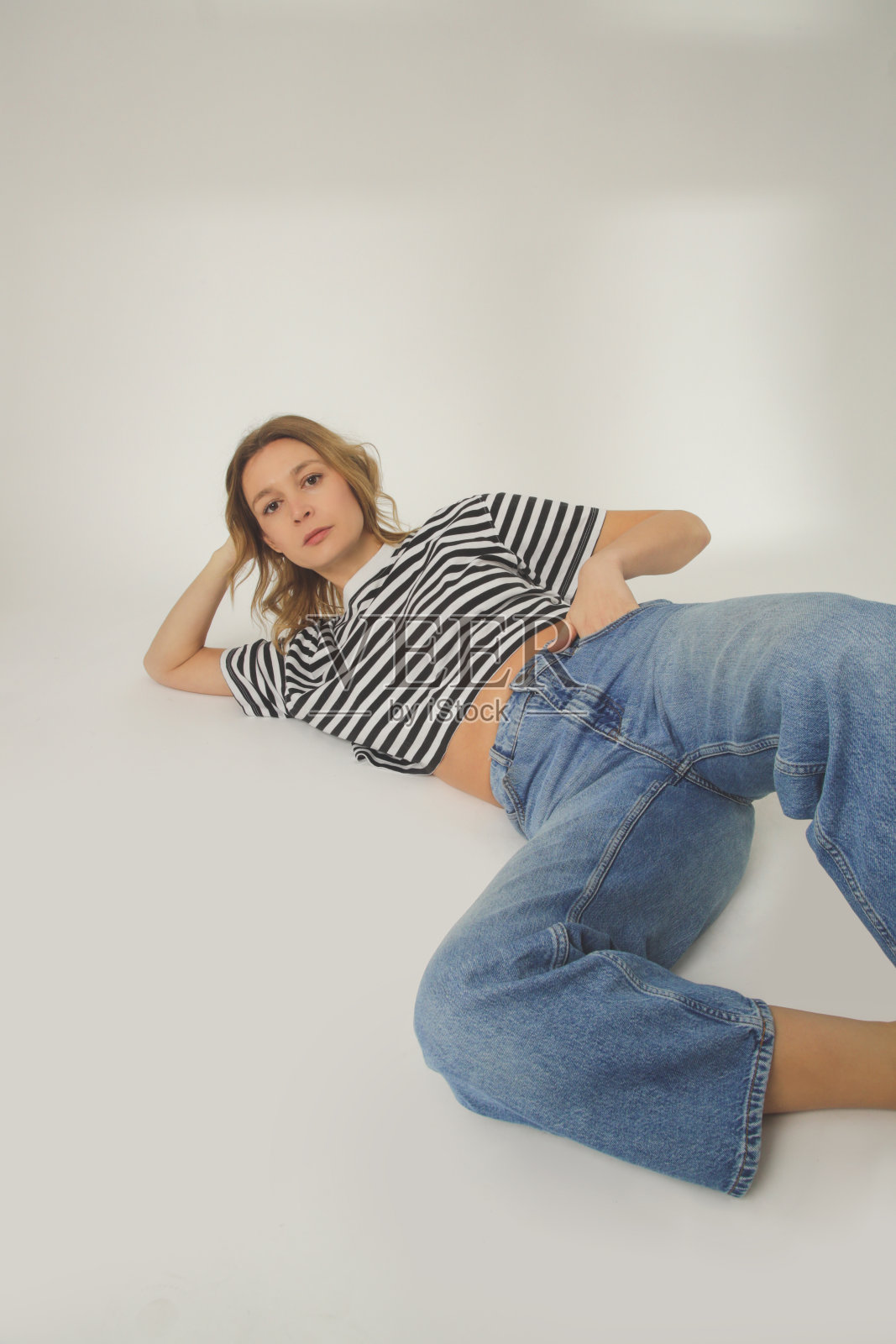 年轻女子的时尚肖像在放松的宽牛仔裤和条纹t恤上的白色背景照片摄影图片