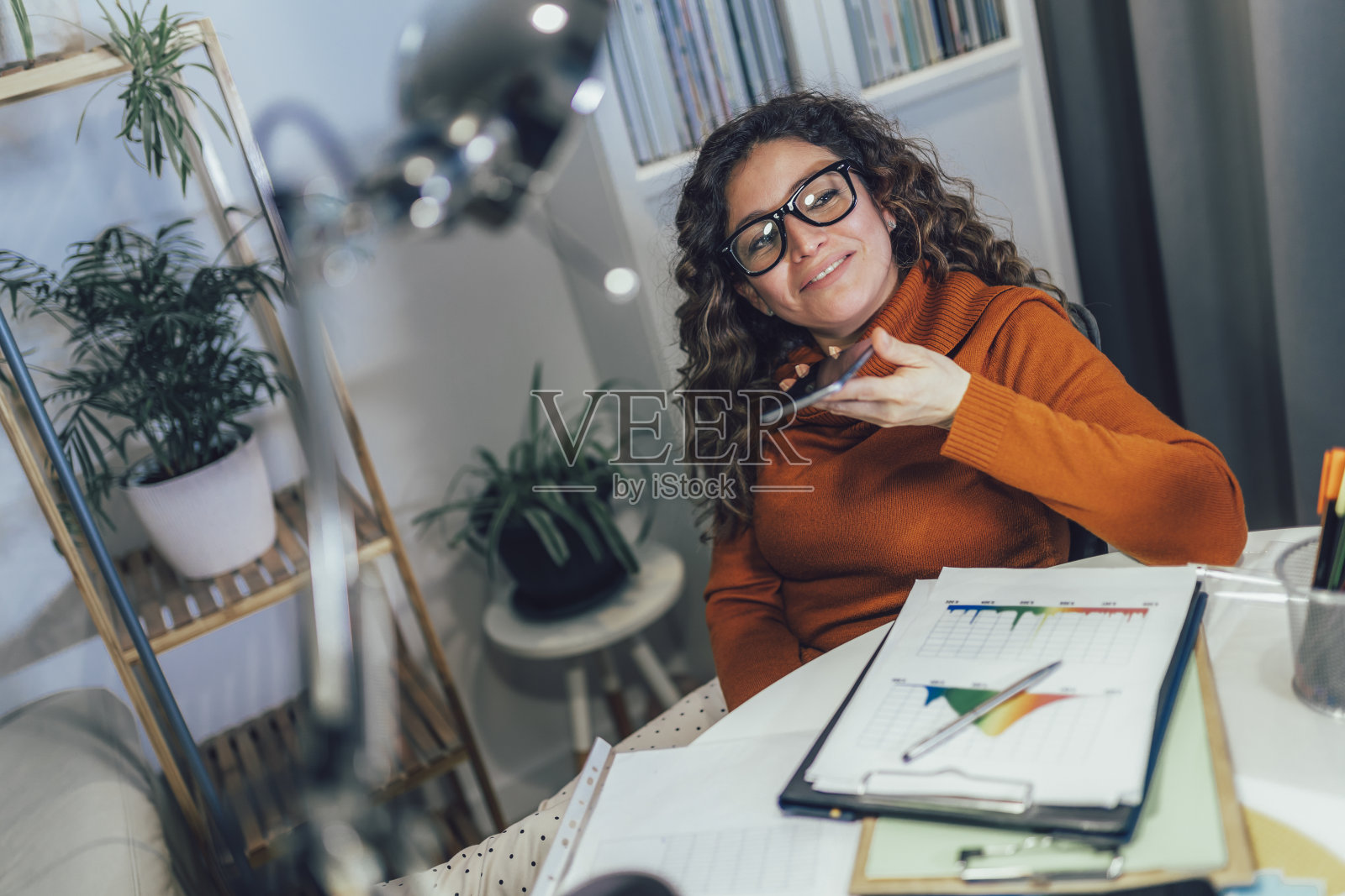 年轻女子使用手机工作，在家里打语音电话。照片摄影图片