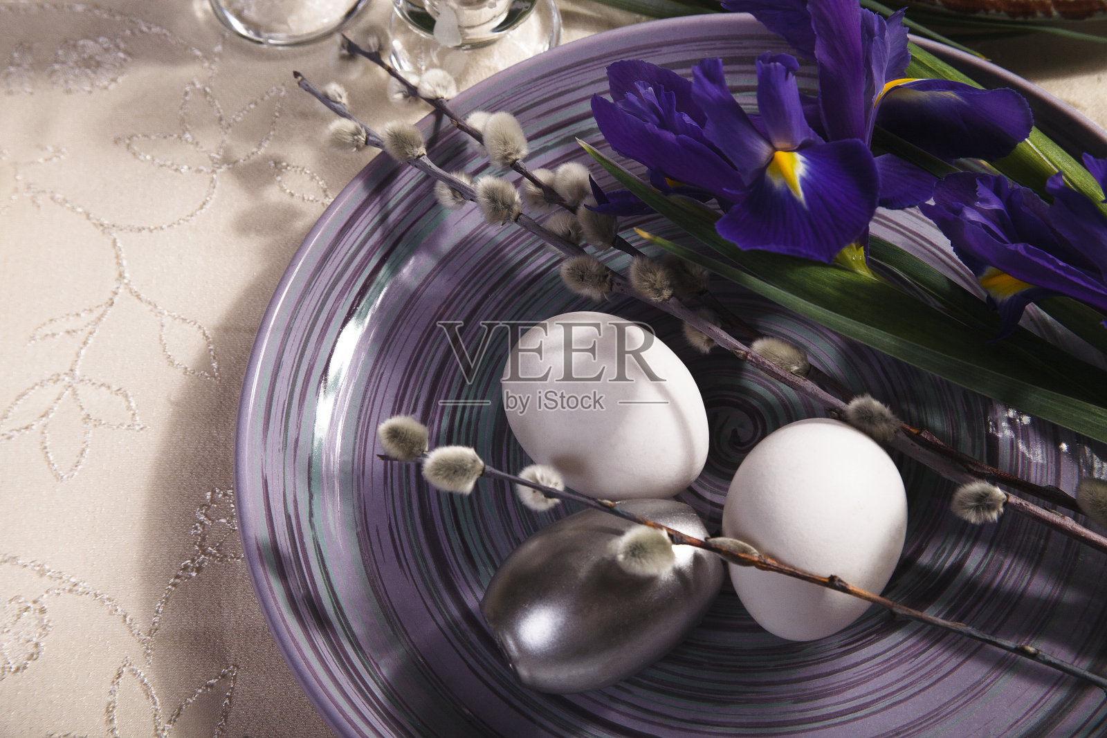 复活节餐桌布置的想法，紫罗兰鸢尾花，柳枝和白色和银色的鸡蛋在紫色的盘子。照片摄影图片