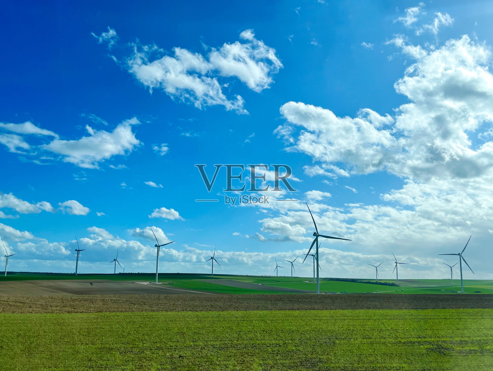 风车的背景是绿色的田野和蓝色多云的天空。用于发电的风力涡轮机照片摄影图片