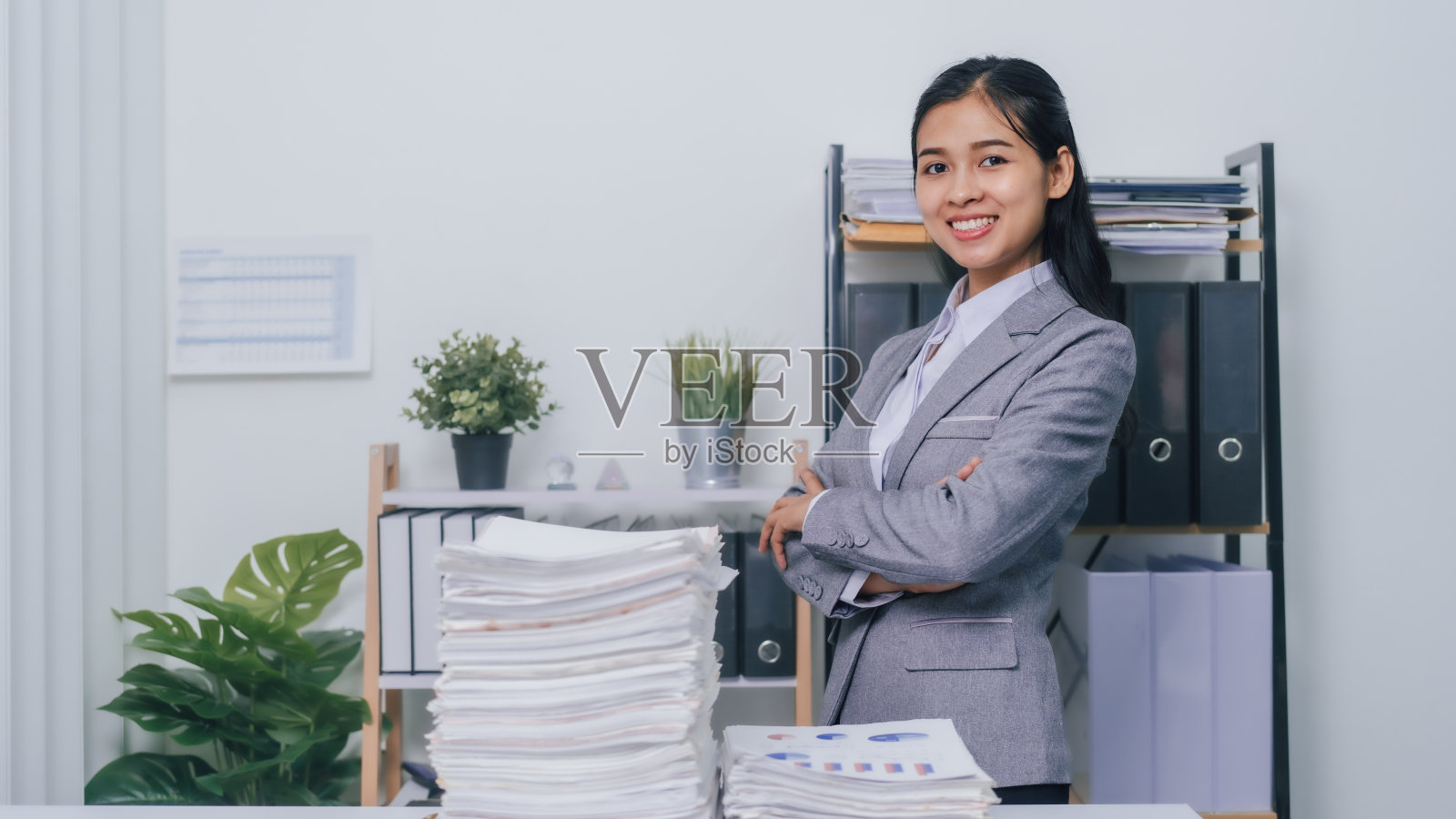 年轻自信的亚洲商业女性办公室工作人员与成堆的文件，未完成的文件记账。照片摄影图片