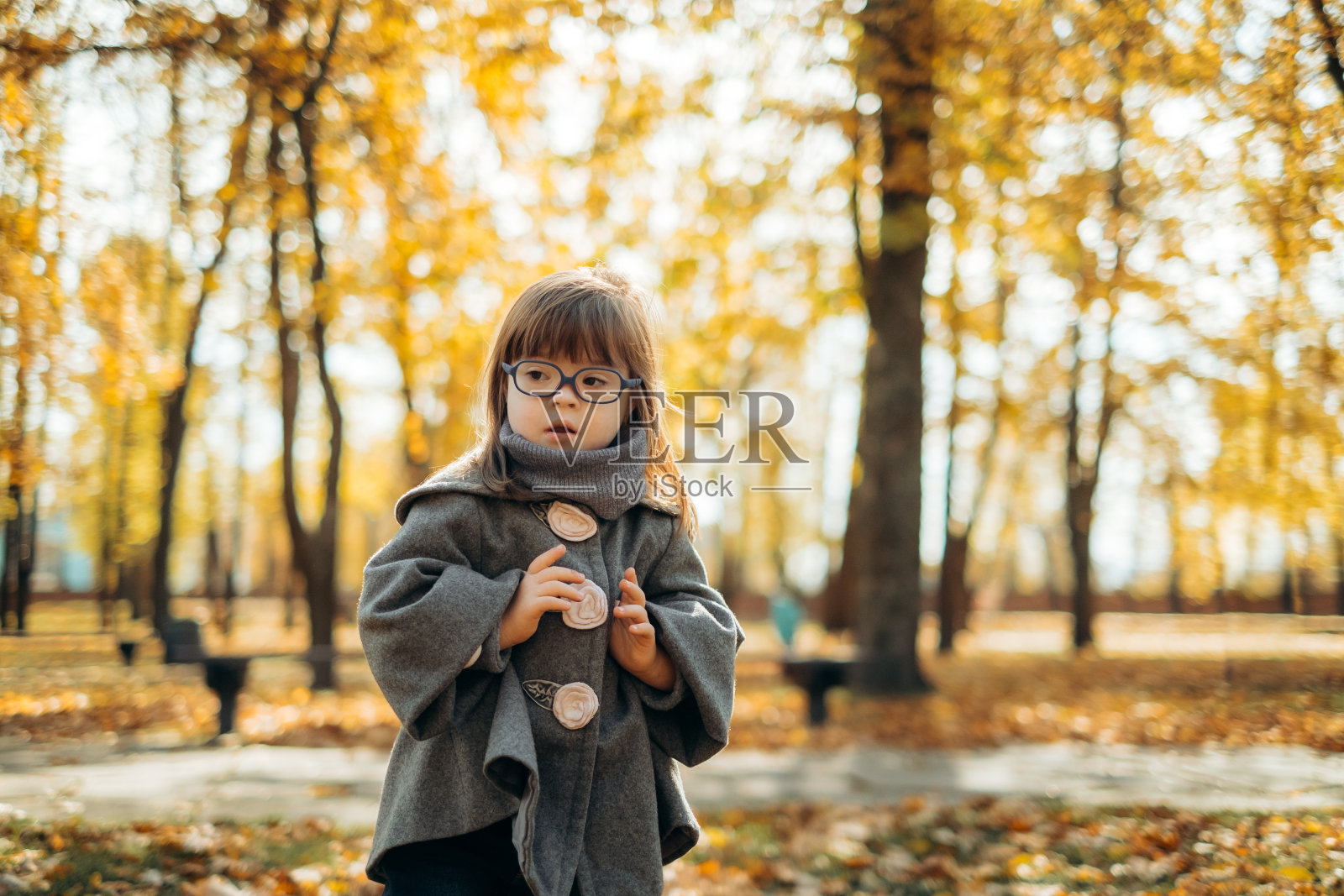 快乐可爱的女孩穿着时髦的外套戴着时髦的眼镜走着笑着，孩子在温暖的秋日公园里享受时光，童年快乐照片摄影图片
