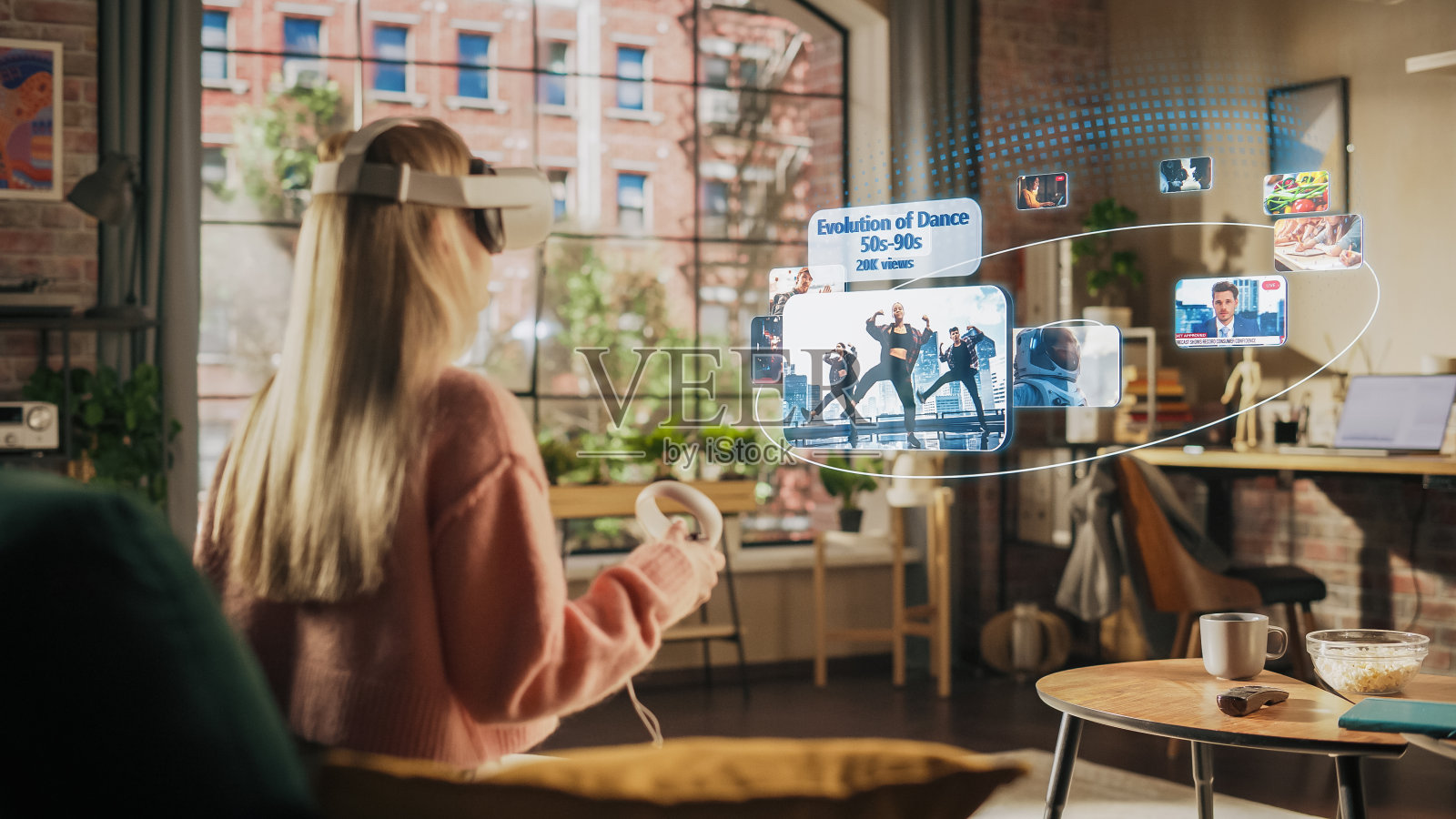 女人坐在家里的阁楼客厅里，使用带控制器的虚拟现实耳机检查社交媒体流媒体应用程序，浏览社交网络提要，喜欢帖子，观看视频照片摄影图片