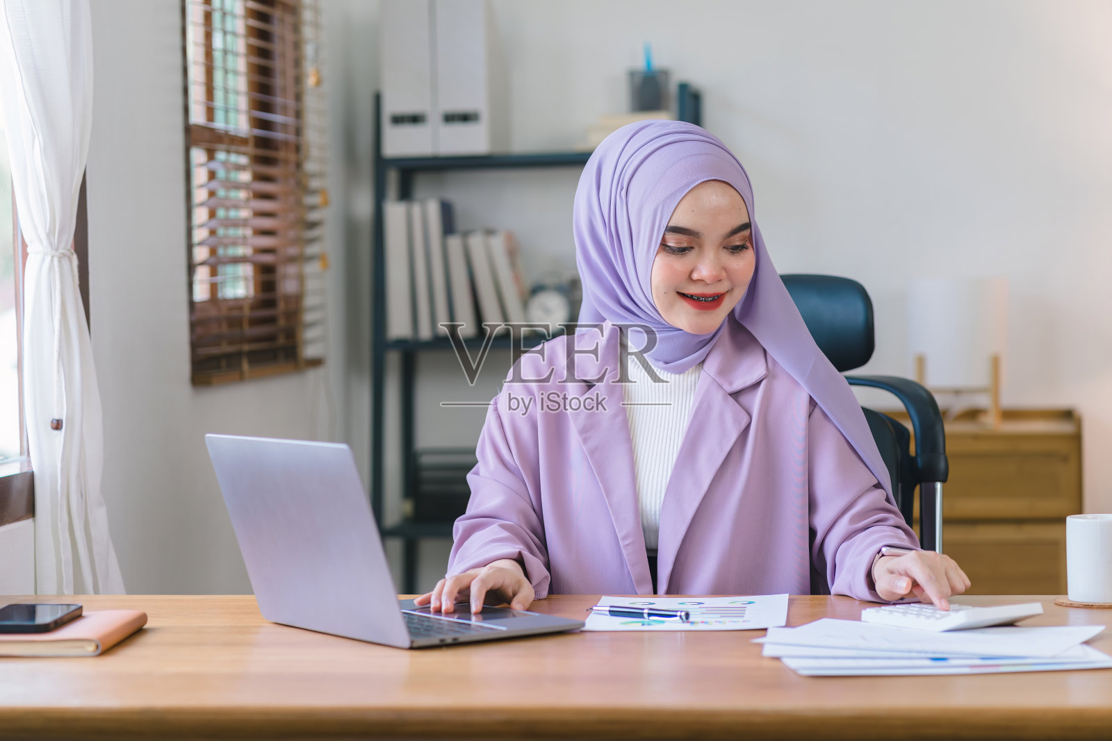 令人惊叹的亚洲穆斯林千禧年女商人戴着紫色头巾在她的家庭办公室工作。照片摄影图片