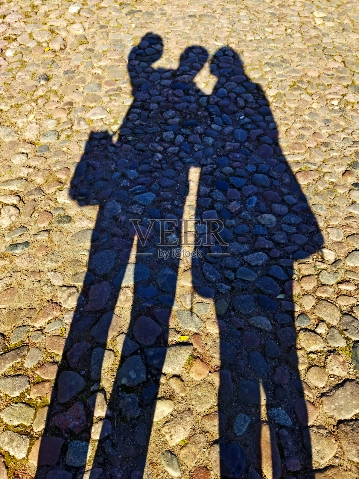 在一个阳光明媚的日子里，两个人的剪影在一条石头路的背景上。照片摄影图片