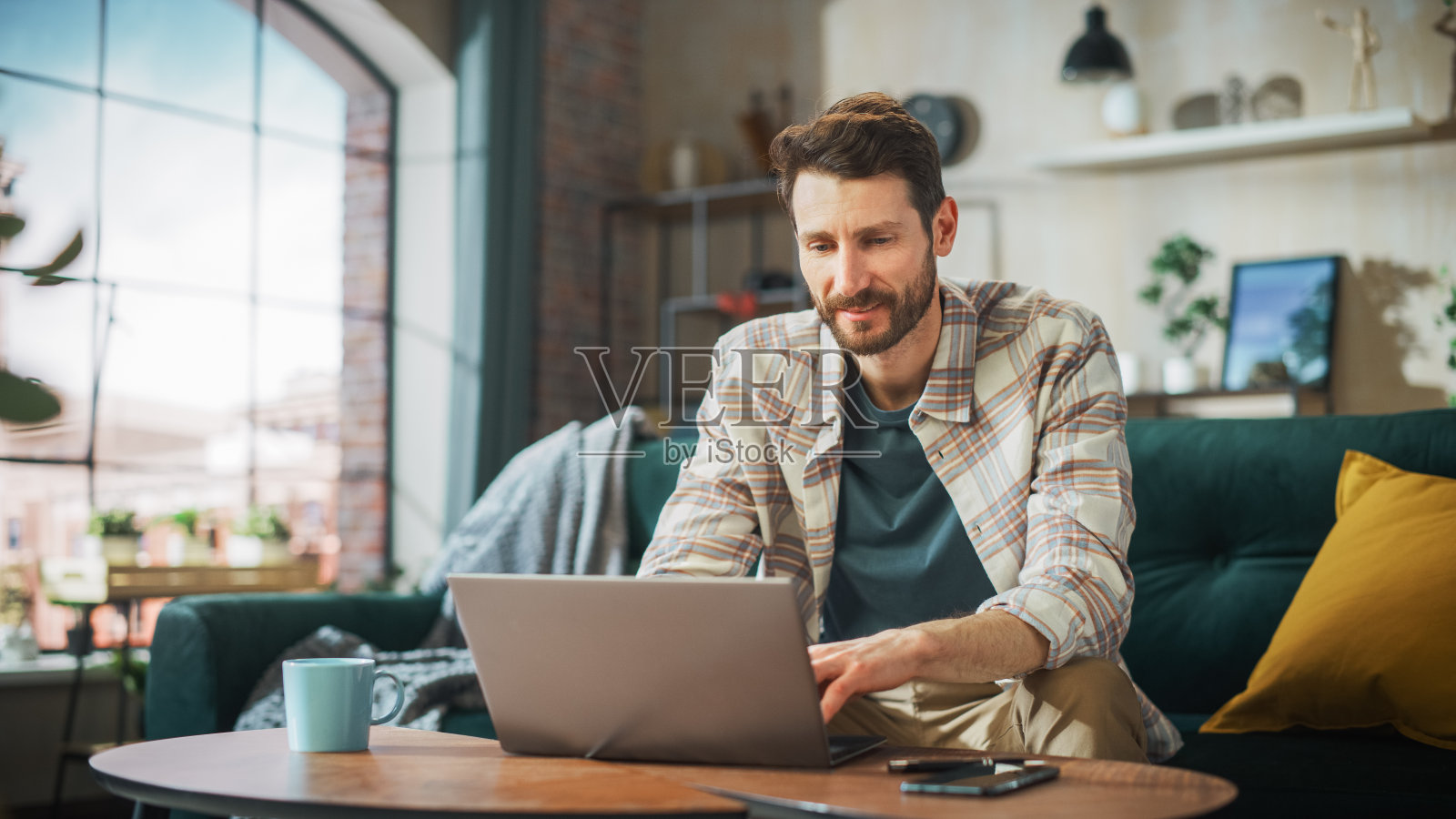 微笑的中年男子在阳光明媚的舒适公寓的笔记本电脑上在家工作的肖像。成功的男性企业家远程进行电子商务项目，网上购物照片摄影图片