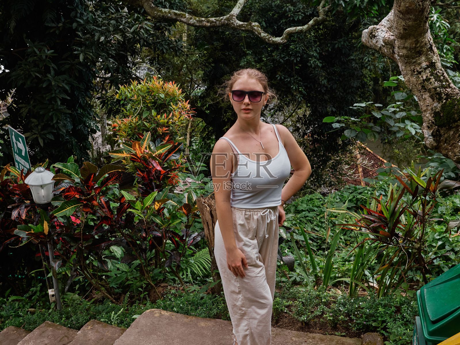 白人妇女与太阳镜摆造型与绿色的树在背景照片摄影图片