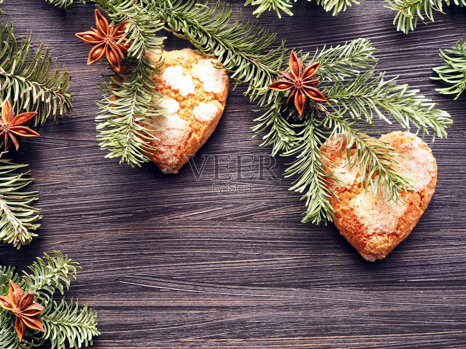 Сookies in the shapes of hearts, decorated on fir branches with star anise on a dark brown wooden background照片摄影图片