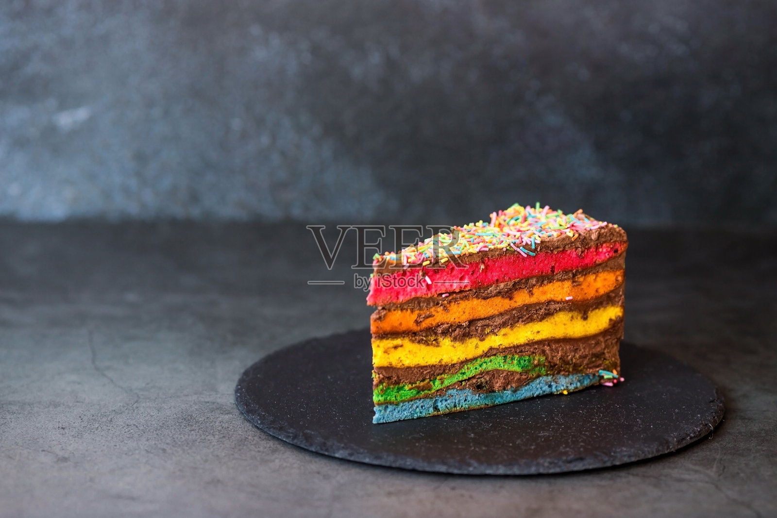 彩虹生日蛋糕装饰着喜庆的蜡烛和五彩纸屑。糖果。五彩缤纷的甜点，在黑色的背景上有彩虹的颜色。照片摄影图片