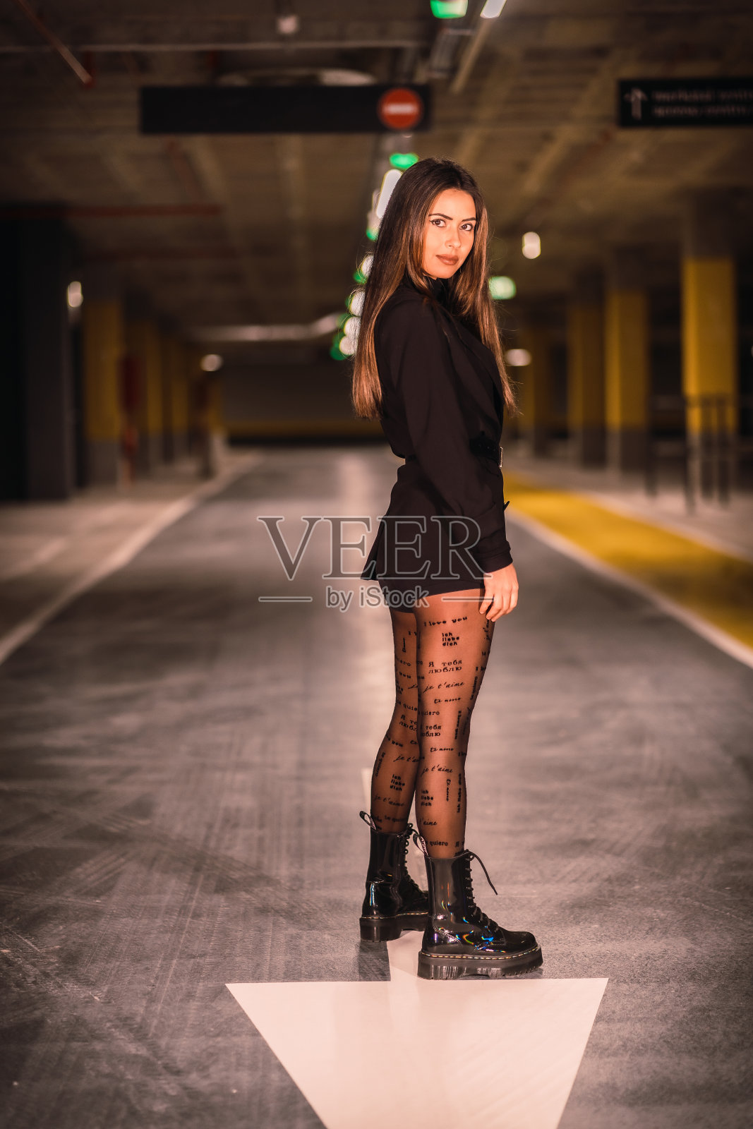 年轻女性穿着黑色夹克，短裤和靴子，在地下停车场摆姿势照片摄影图片