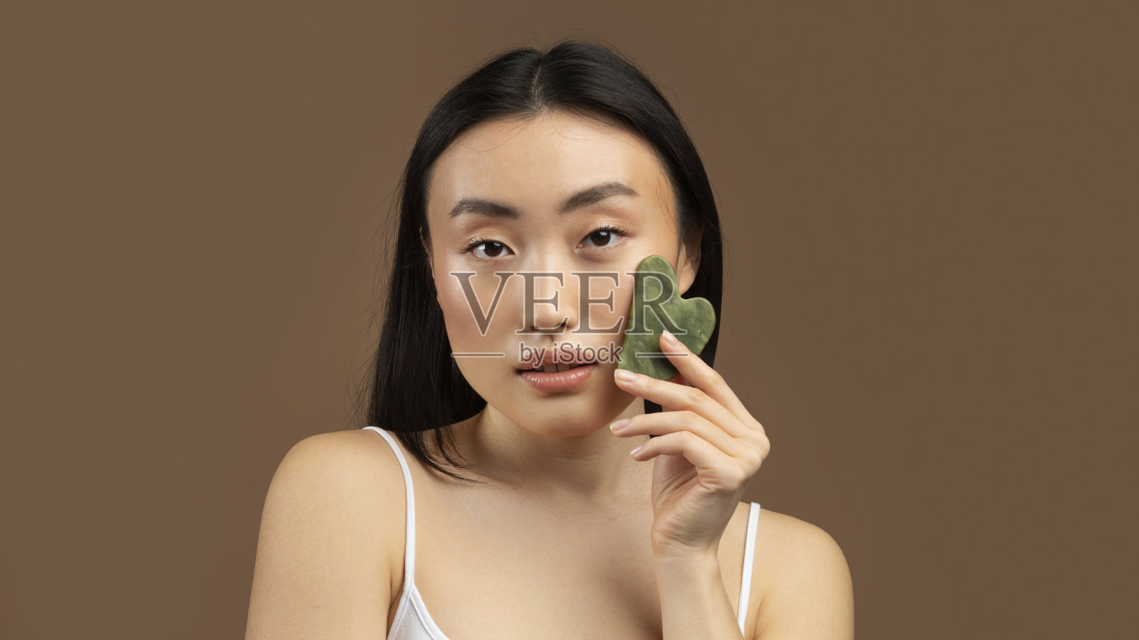 韩国女士按摩面部由刮刀石英石护肤，在棕色背景，全景照片摄影图片