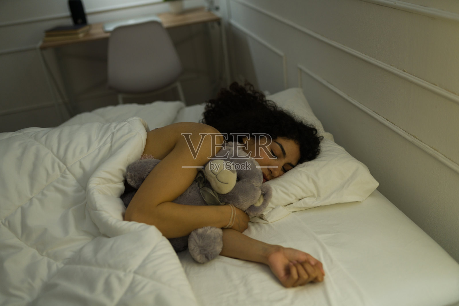 微笑的女人抱着她的泰迪熊睡觉照片摄影图片