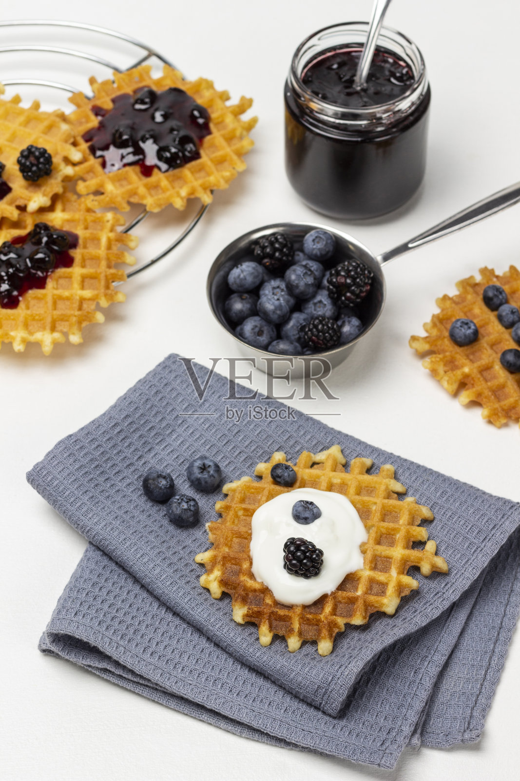 华夫饼加浆果和酸奶，放在灰色餐巾上。一罐果酱。照片摄影图片