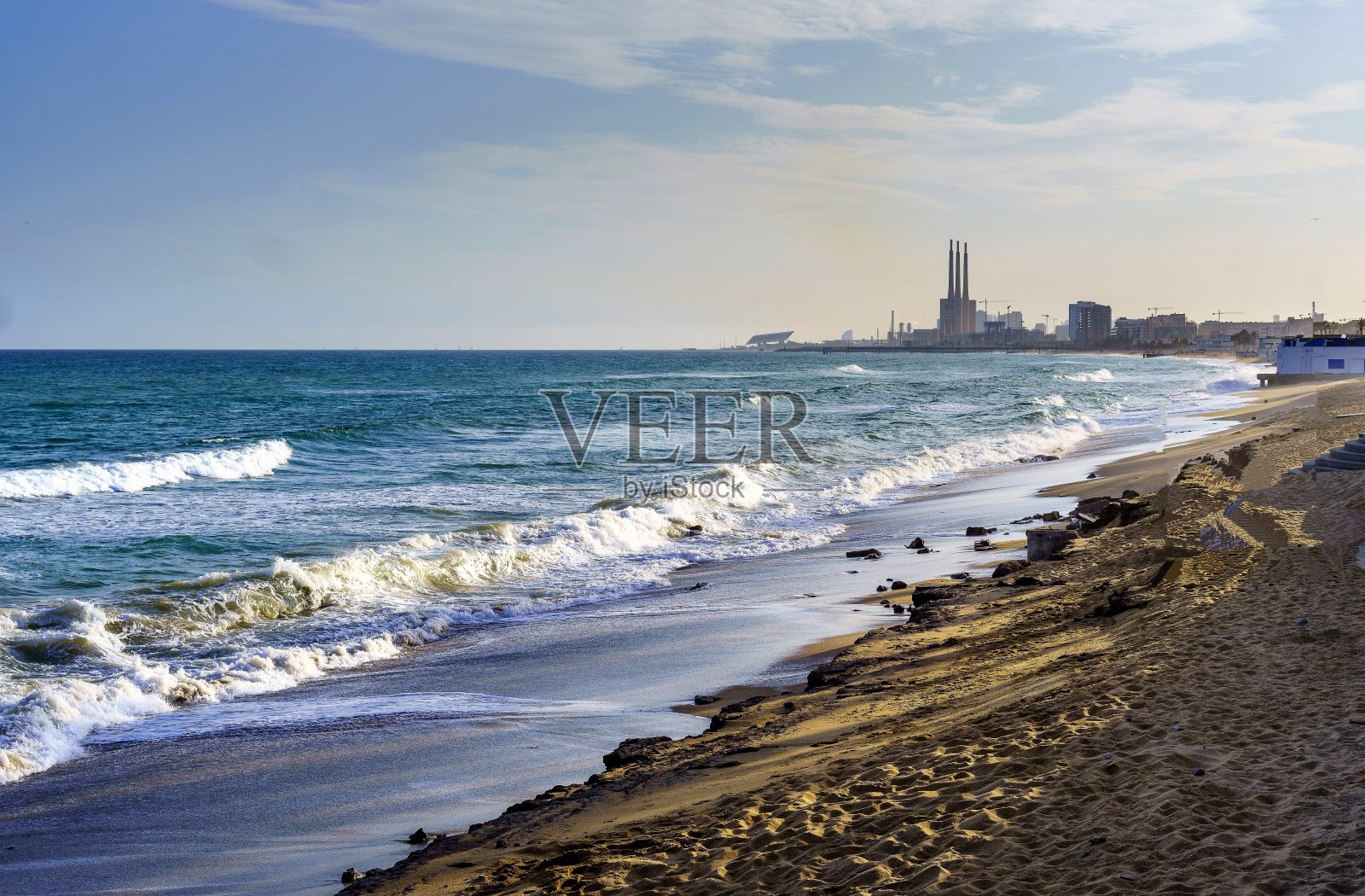 太阳在西班牙巴达洛纳的地平线上落下，反射出田园诗般的海湾的波浪。冲浪者利用风和防波堤的优势，欣赏大自然的美丽。照片摄影图片