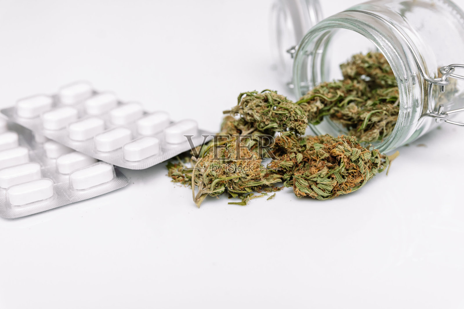 干燥和修剪的大麻芽在玻璃罐外，旁边是白色背景的药丸。照片摄影图片