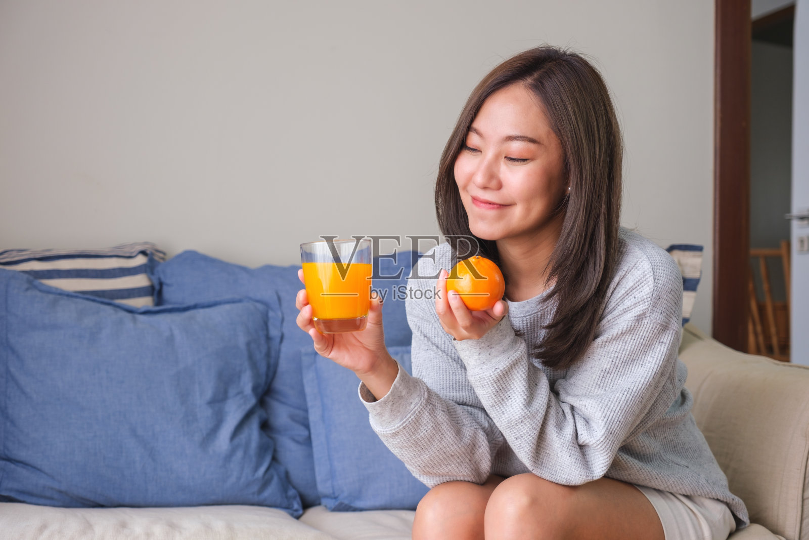 一个年轻女子在家里拿着一个橙子和一杯新鲜的橙汁照片摄影图片