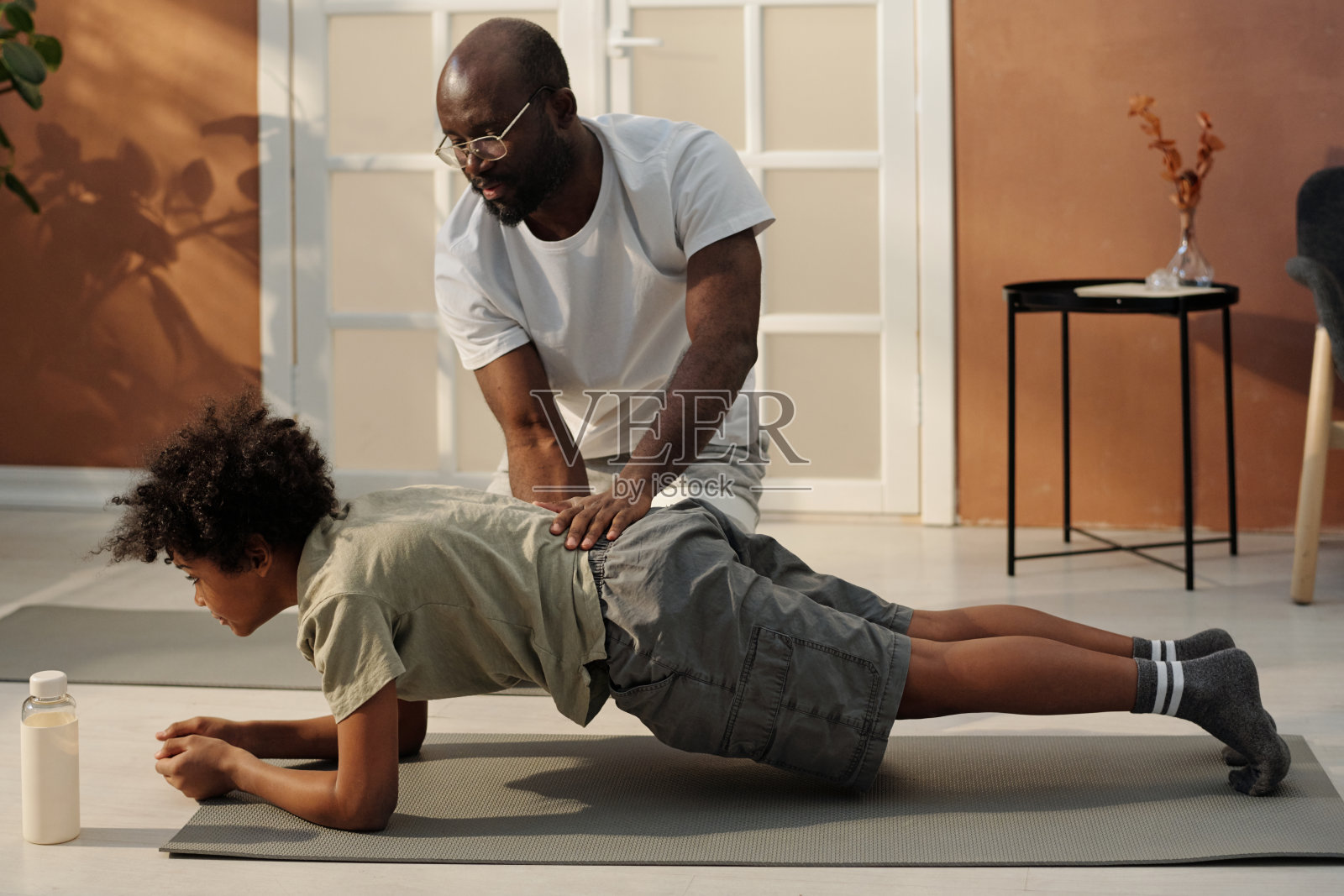 年轻的非裔美国人在运动服帮助他的儿子平板支撑照片摄影图片