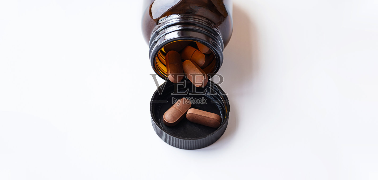 维生素胶囊从白色的琥珀色玻璃瓶中溢出。天然保健品，治疗和支持健康。照片摄影图片