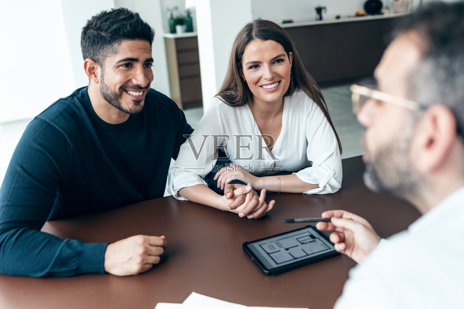 英俊的房地产经纪人在电子平板电脑上展示房子计划，同时在办公室与夫妇谈论购买房子。照片摄影图片