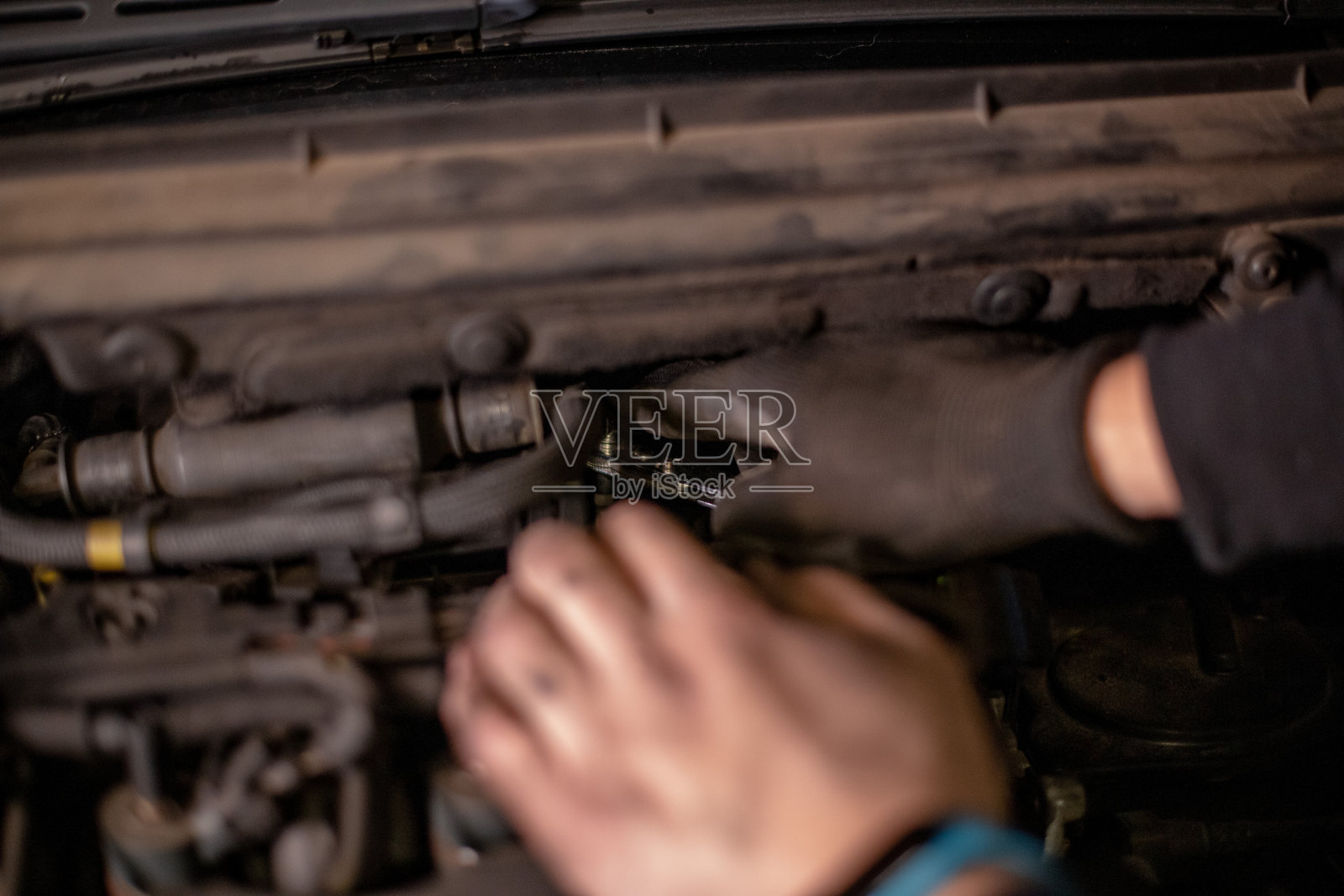 年轻的自动修车。他戴着手套，用着手工工具。他的手是焦点，在背景打开的汽车引擎盖。侧视图，近一点照片摄影图片