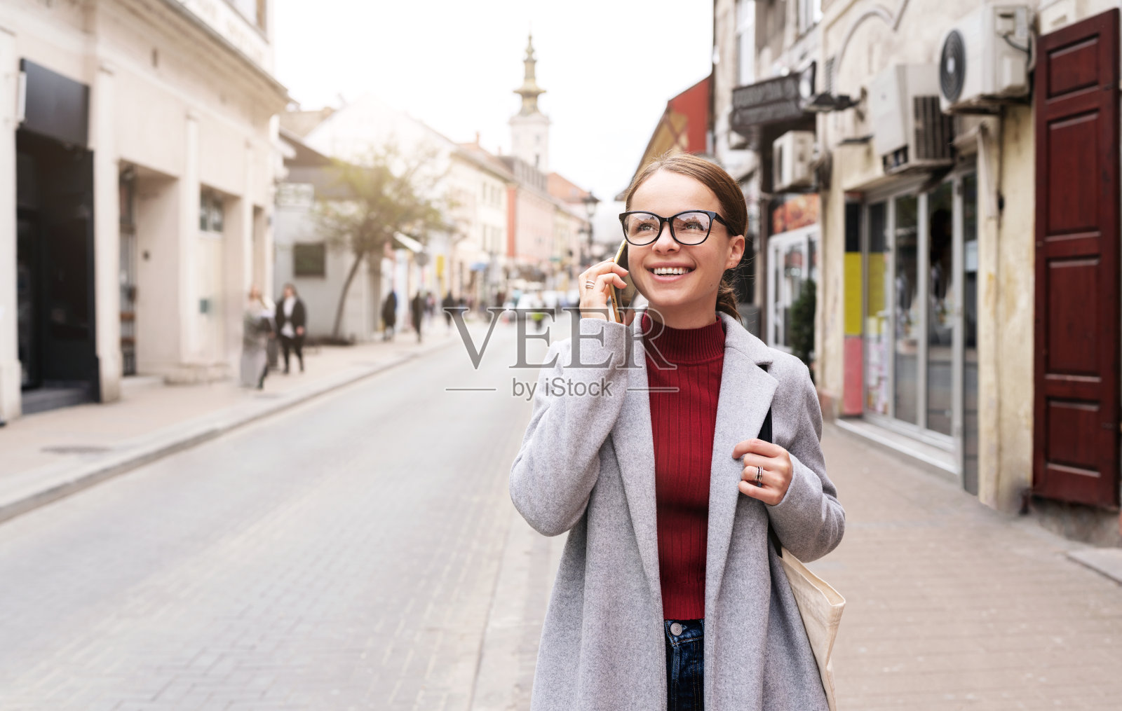 一名戴眼镜的女子站在城市街道上打电话。照片摄影图片