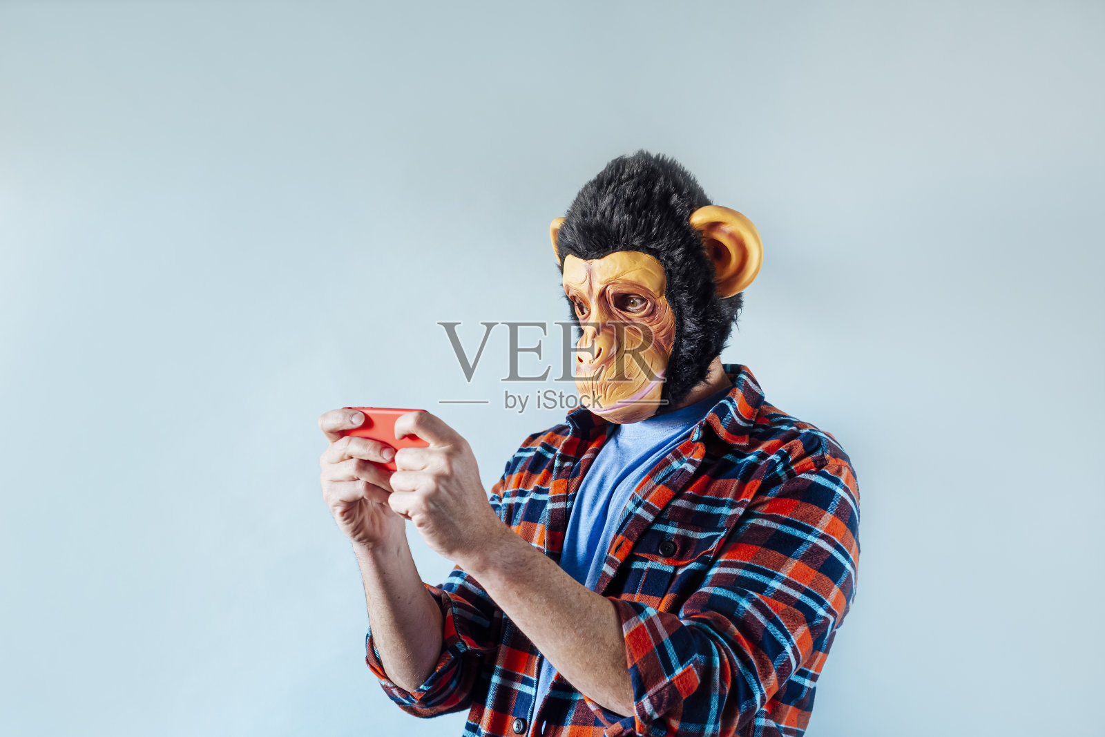 戴着猴子面具的男子使用智能手机。照片摄影图片
