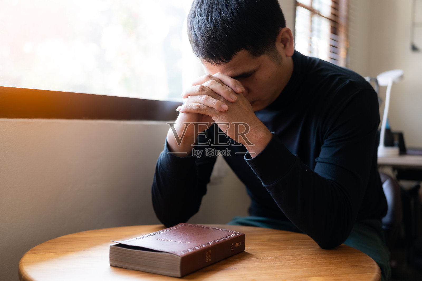 一名男子拿着一本《圣经》放在桌子上，窗外的灯光象征着希望和上帝。信仰、灵性和宗教的概念照片摄影图片