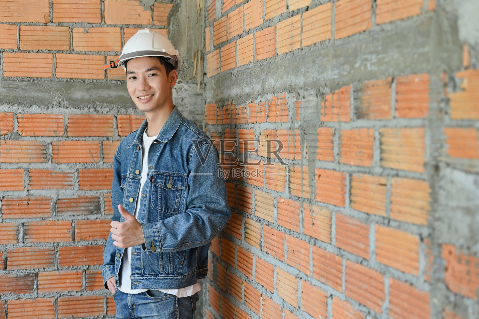 年轻的男性建筑工程师或建筑师在建筑工地的蓝图，看着镜头。照片摄影图片