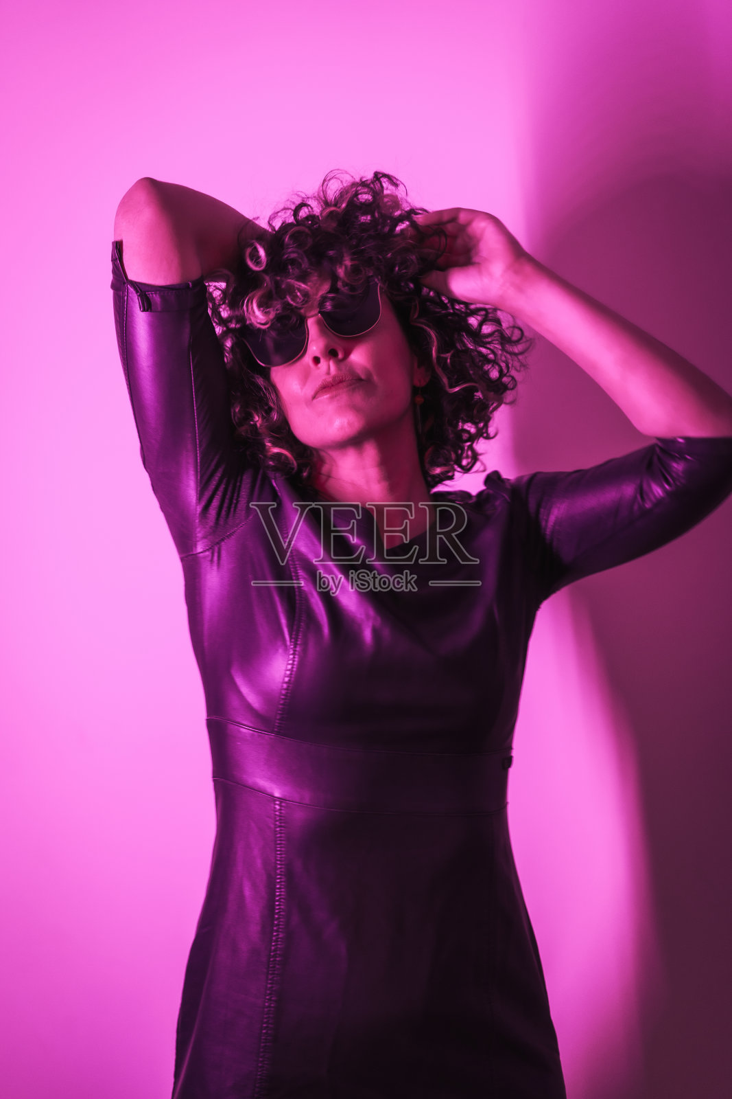 垂直拍摄一名戴着墨镜的白人卷曲女性，在派对气氛中举起双手照片摄影图片