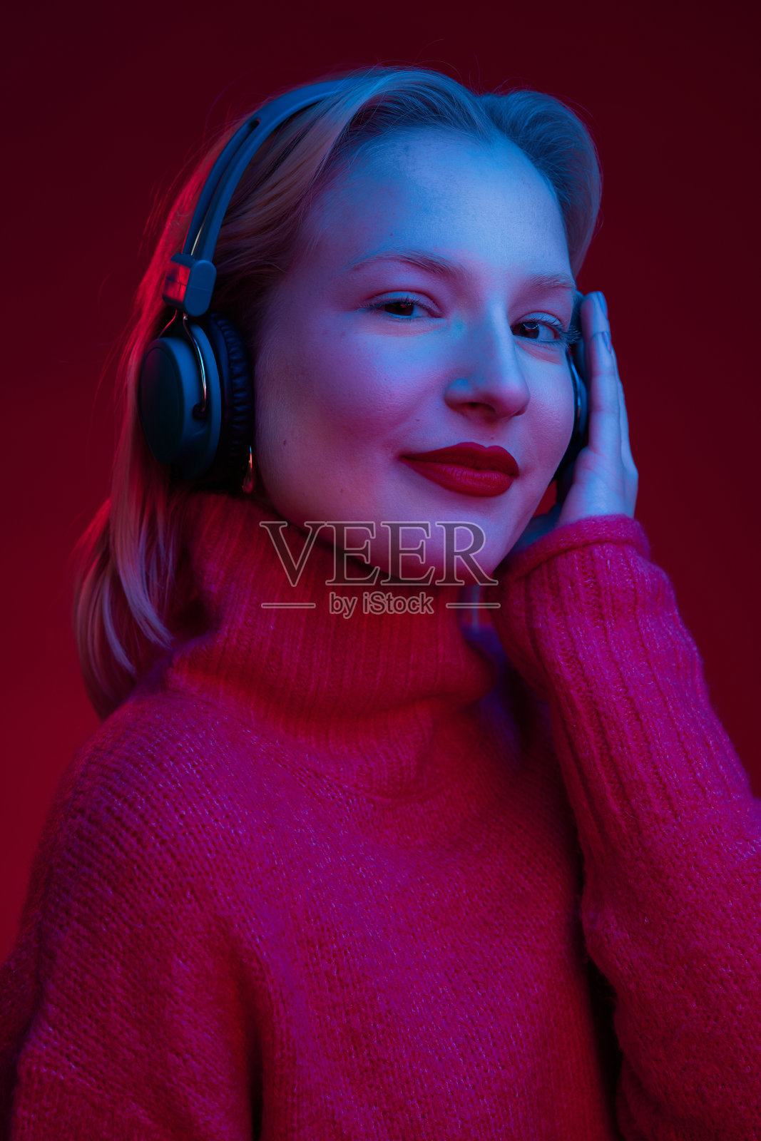 一名快乐的女子戴着wifi耳机听着音乐，对着镜头微笑。霓虹灯点亮，孤立在洋红色的背景上。洋红色万岁，年度流行色。照片摄影图片