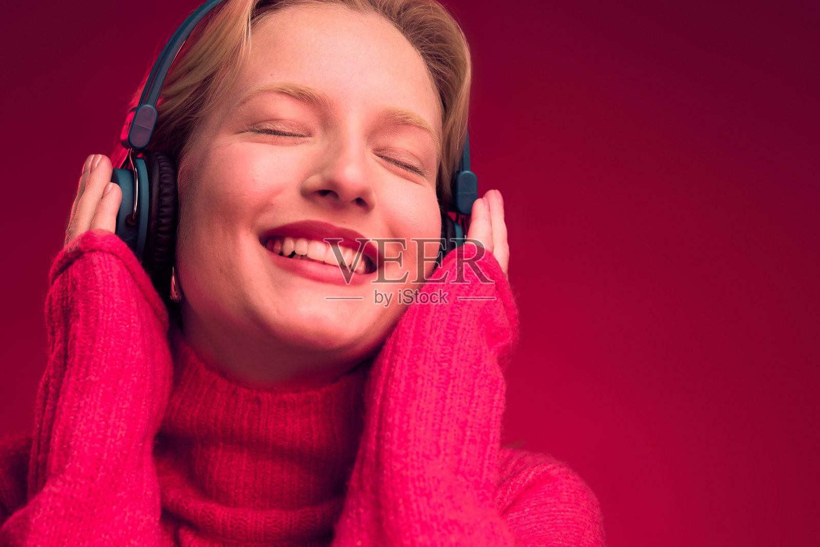 一个美丽的女人的肖像享受音乐耳机，而站在洋红色背景孤立。年度流行色。照片摄影图片