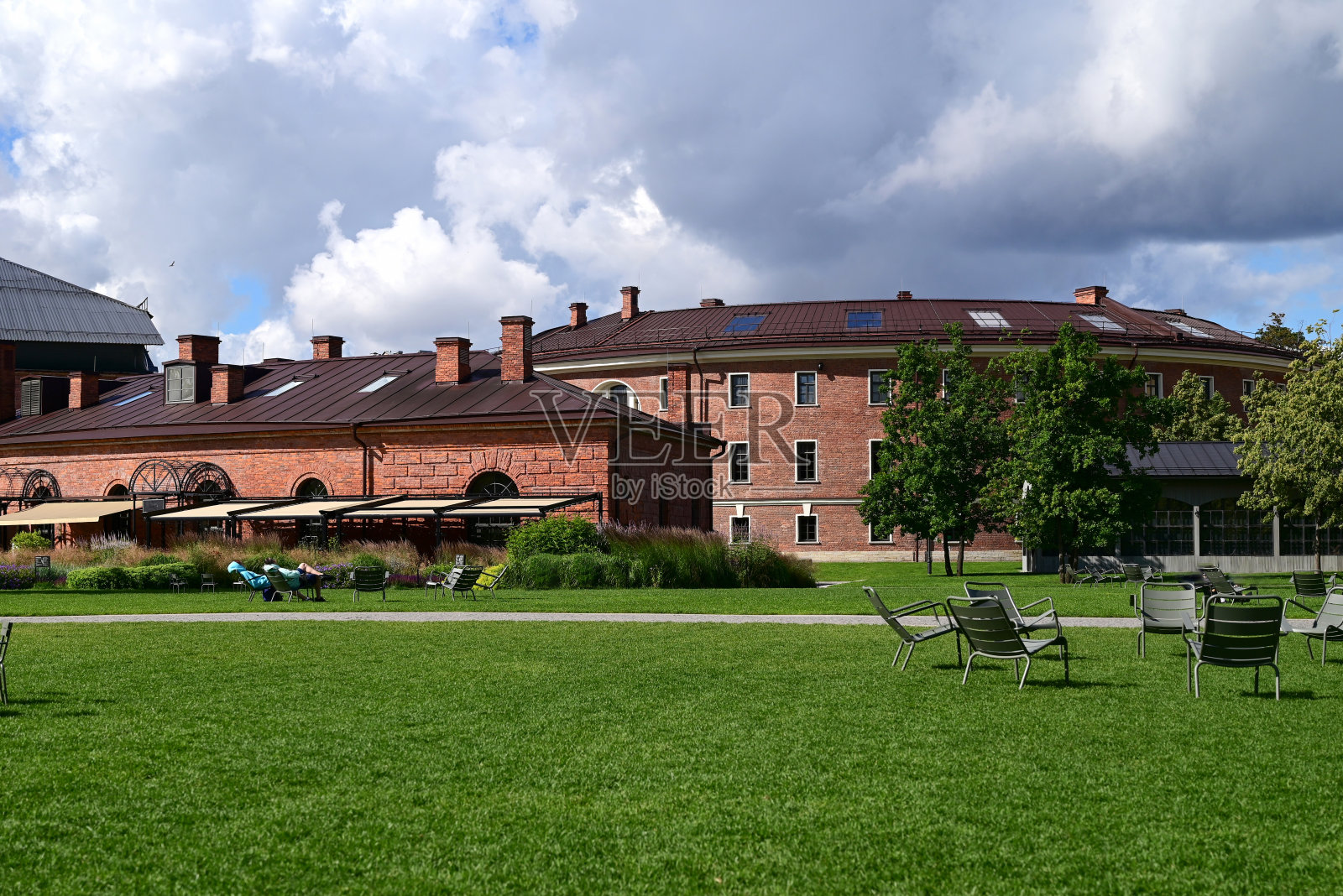 迷人的女性在眼镜，条纹t恤和黑色牛仔裤坐在椅子上交叉她的腿在另一个。迷人的女人在户外享受阳光和温暖的一天。从生活中获得乐趣。照片摄影图片