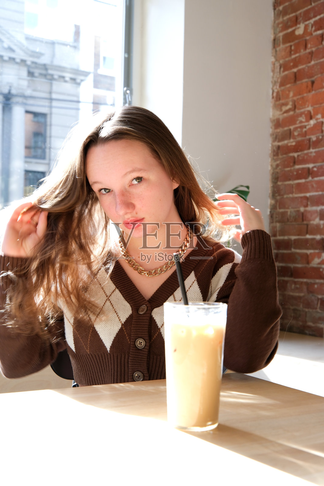 可爱的女孩少年背景的窗口在咖啡馆直发在桌子上的咖啡杯牛奶和冰黑色管喝棕色夹克与菱形美丽的年轻的脸照顾自己照片摄影图片