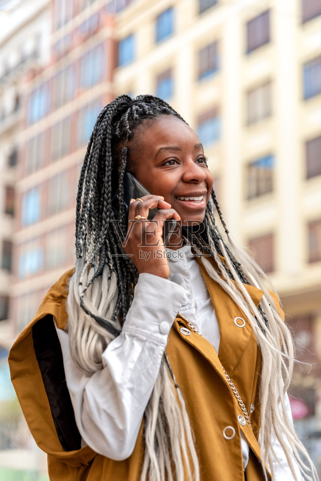 一个微笑着梳着辫子的非裔美国女人一边走在城市里一边打电话照片摄影图片