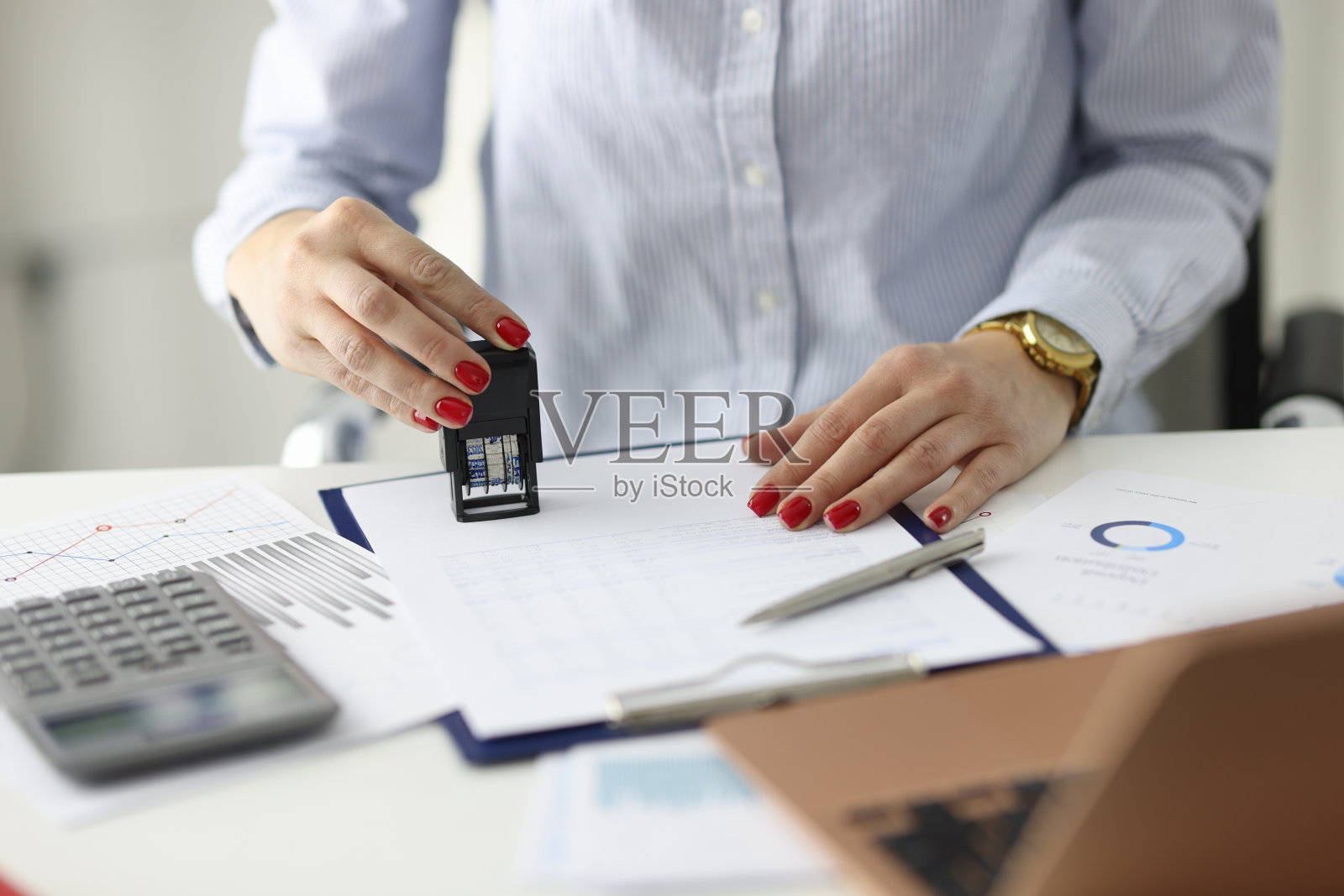留着红色指甲的女人在办公室的文件上盖章照片摄影图片