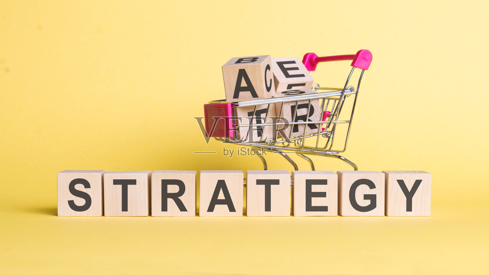“战略”一词在木块上，黄色背景上有一个购物车。照片摄影图片