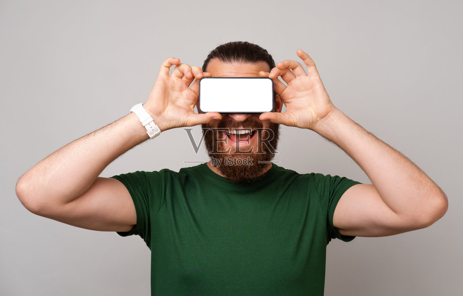 欣喜若狂的大胡子男子用空白屏幕的手机遮住眼睛。照片摄影图片