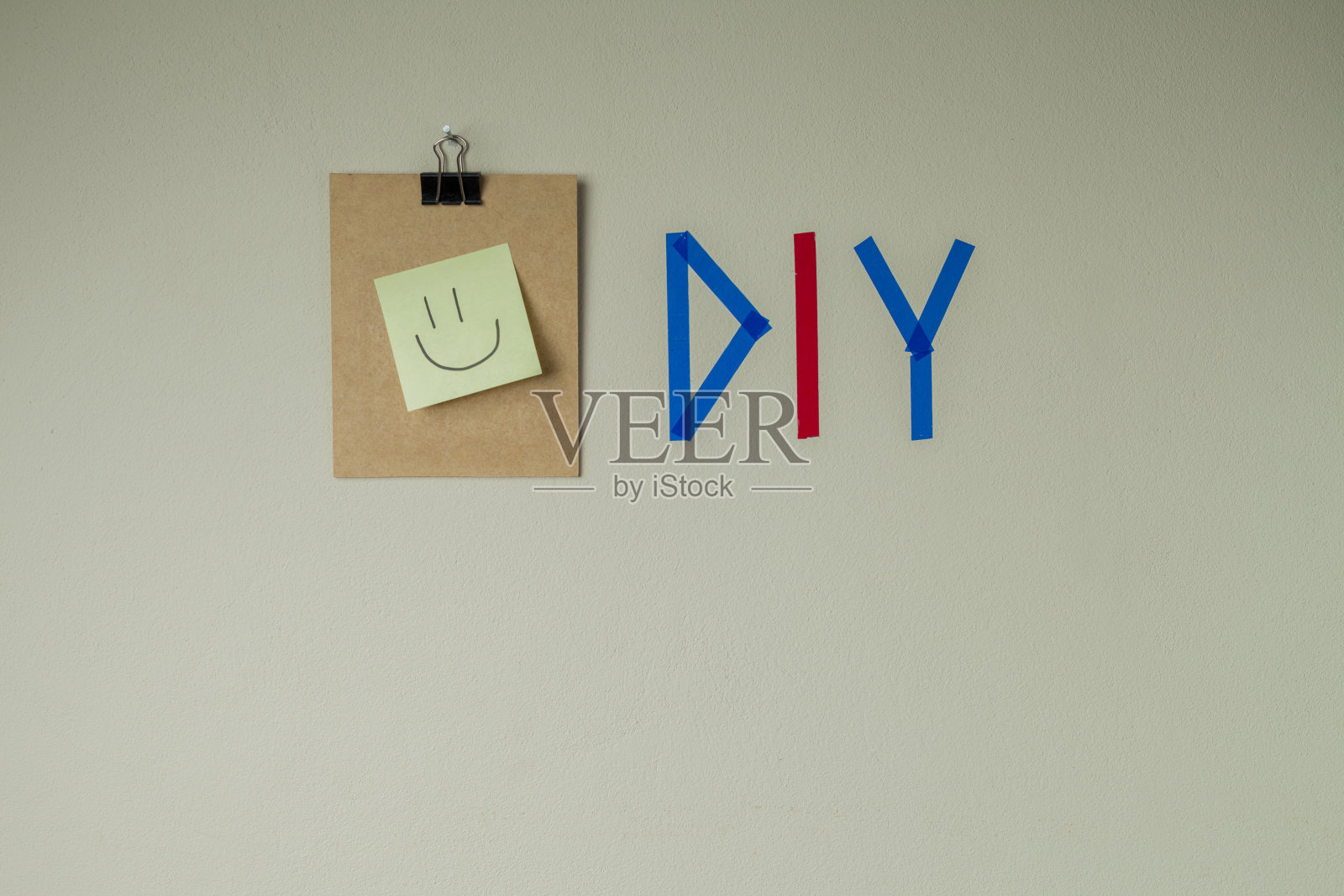 用彩色胶带在墙上DIY写字，旁边有一个剪贴板和一个笑脸笔记贴纸。照片摄影图片