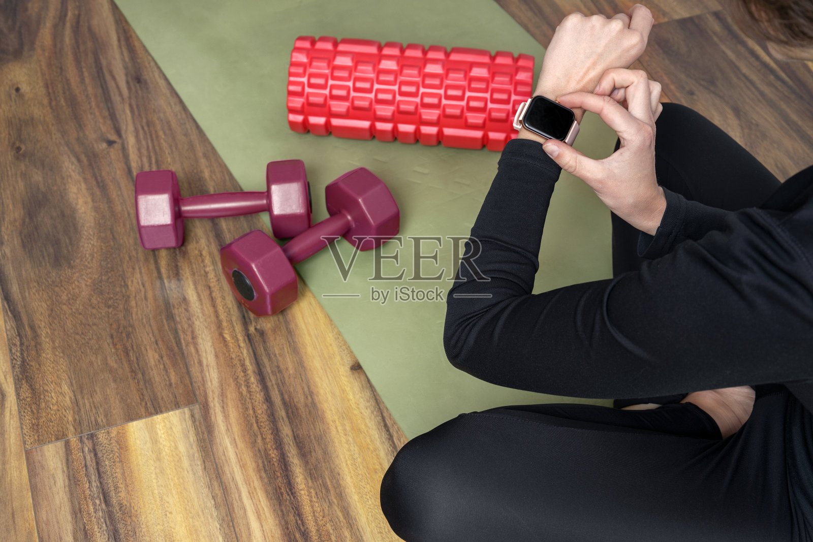 一名女子穿着黑色运动服，坐在垫子上，在训练前使用智能手表照片摄影图片
