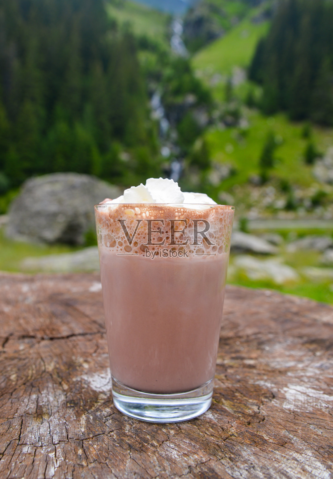 一杯美味的热可可，配上鲜奶油，背景是山上的瀑布照片摄影图片