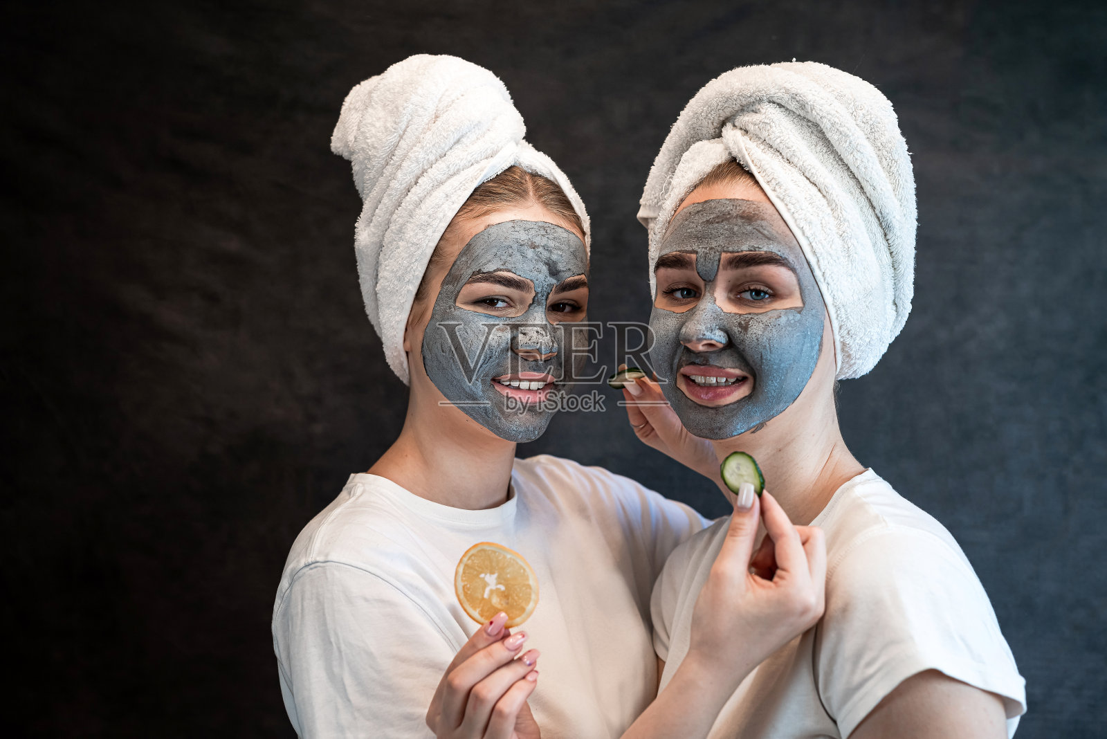 两个快乐的女人姐姐穿着白色浴巾，敷着美容面膜，拿着橘子片照片摄影图片