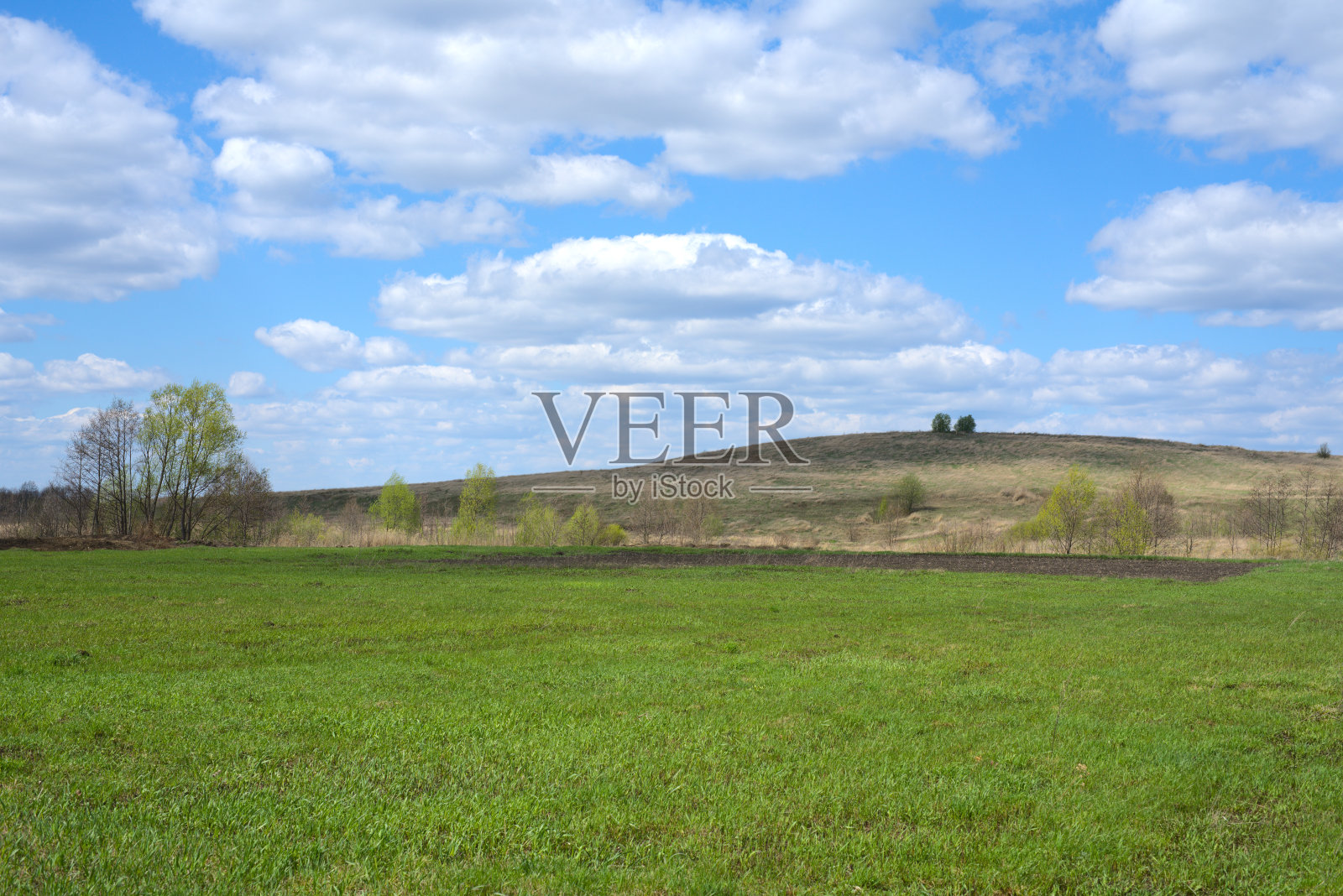 一片绿草地，蓝天白云。远处有一座山。晴朗的春日照片摄影图片