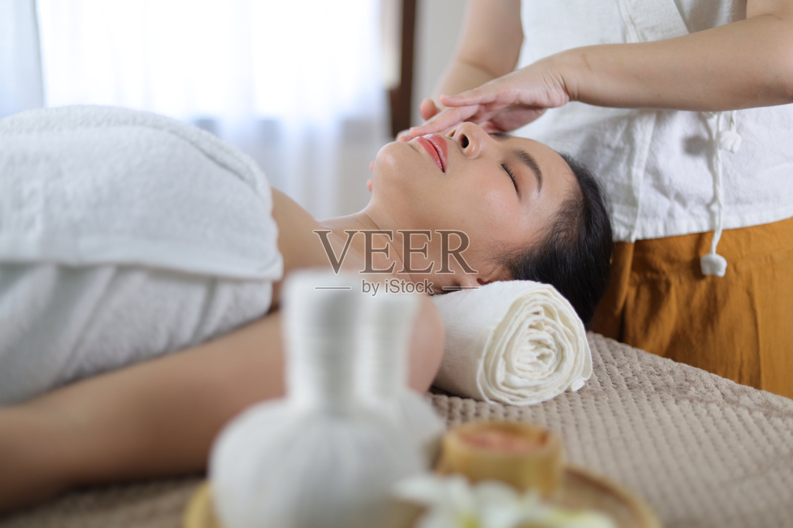 放松的亚洲女子在水疗沙龙接受美容按摩。照片摄影图片
