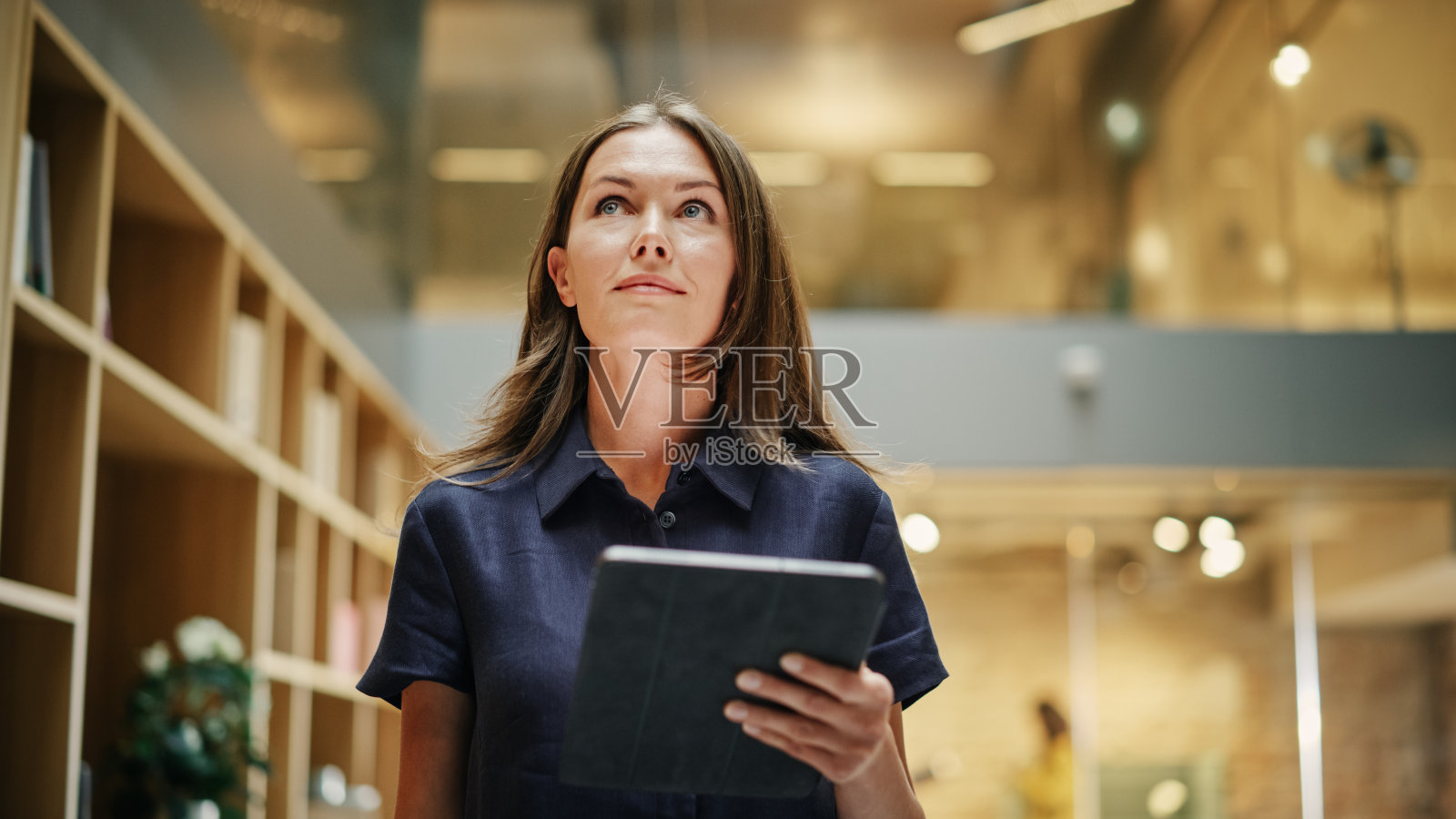 一个女CEO在平板电脑上做笔记的特写镜头。一个白人妇女穿过公司办公室大厅的肖像，微笑着，看起来很自信。低角度照片摄影图片