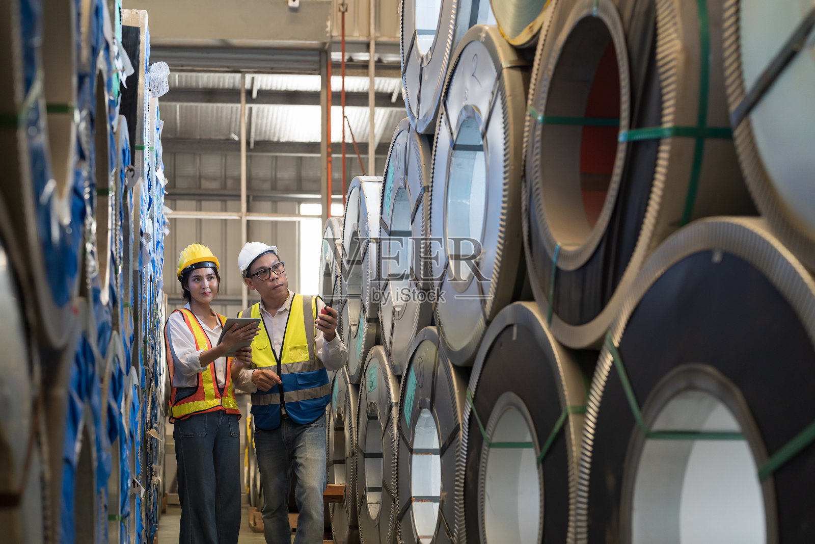 金属制品制造，原材料仓库。亚洲男女工人在工厂检查金属板材的质量卷。一组检验员在仓库检查金属片照片摄影图片