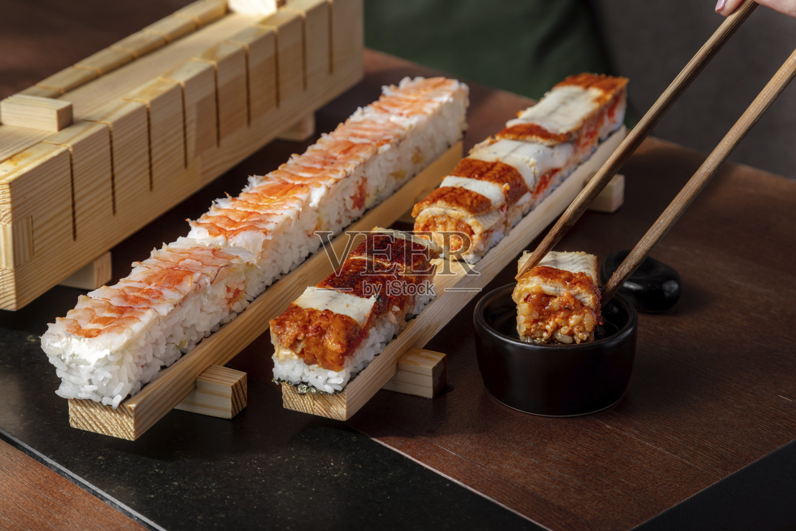 准备用米饭、虾、鳗鱼、鱼杂、鱼杂鱼子酱和酱汁做的卷，酱汁放在桌子上的机器里，酱汁放在酱碗里，由一个男人扮演食物棍的角色照片摄影图片