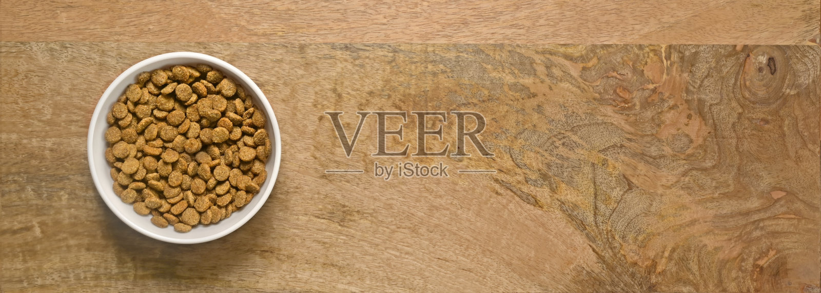 白色的碗里装满了干宠物食品，背景是木制的。带有复制空间的全景图像。照片摄影图片