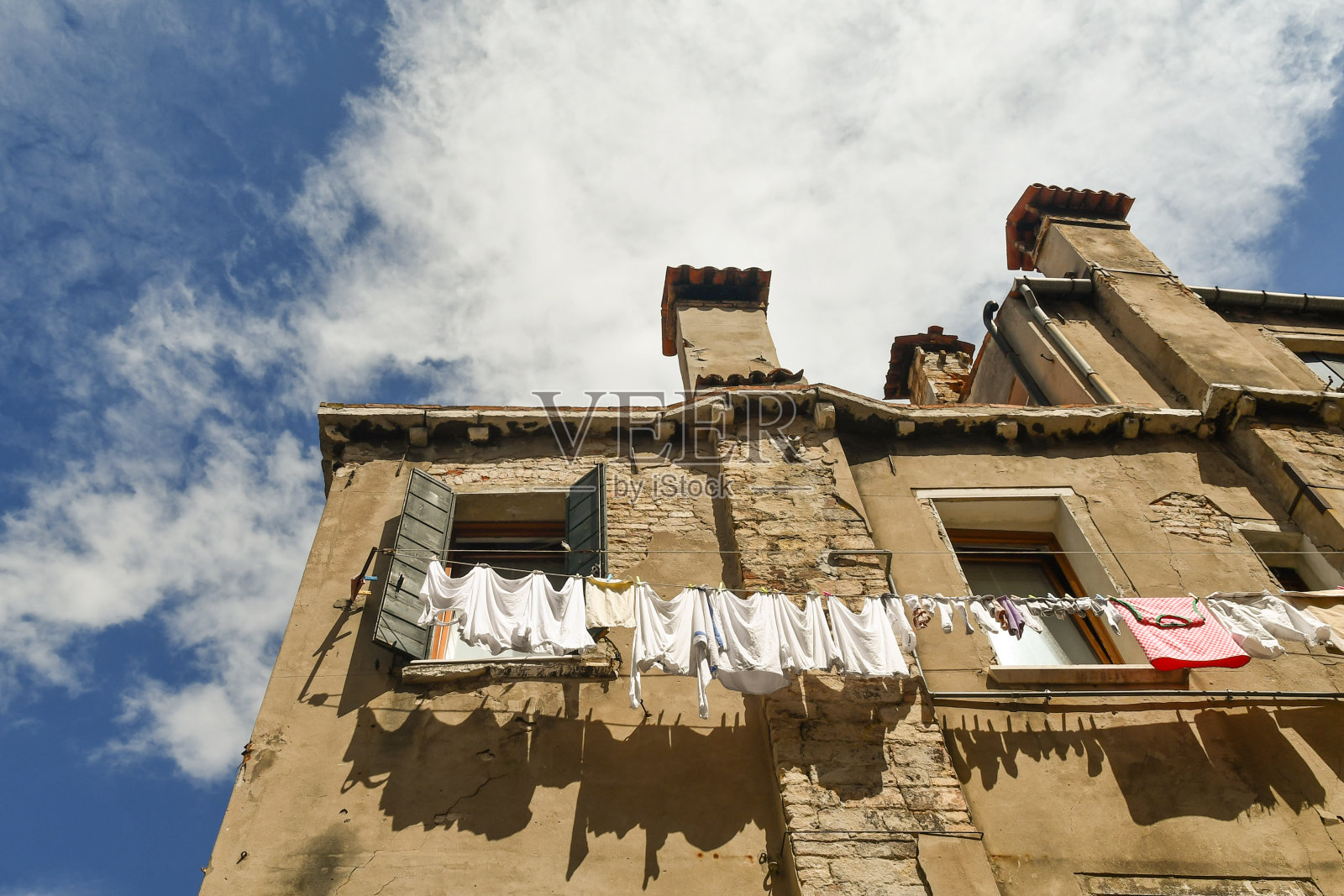 意大利威尼斯，威尼托，一座威尼斯老房子的低角度外立面，窗外有晾衣绳，烟囱映衬着蓝天照片摄影图片