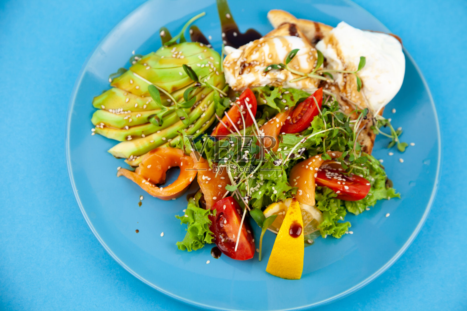 蓝色盘子里的早餐。鳄梨、红鱼鲑鱼、鸡蛋、芝麻、亚麻籽、西红柿、微型蔬菜沙拉。蓝色背景，有文字空间。健康食品，有益健康的食品。鳄梨沙拉。照片摄影图片